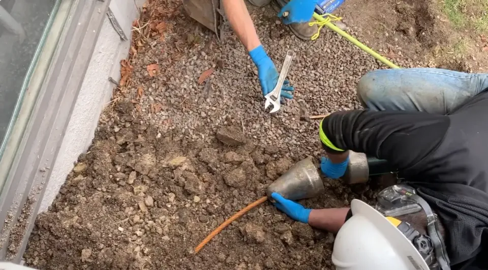 Gloved workers positioning a metal pulling head and cable at an excavated pipe opening.